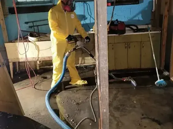 Technician in protective suit and respirator extracting a sewage backup in a Sandy basement